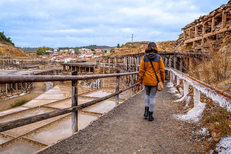Woman exploring the ancient salt flats of anana, finding herself immersed in the historical landscape with traditional salt pans and a captivating village in the background