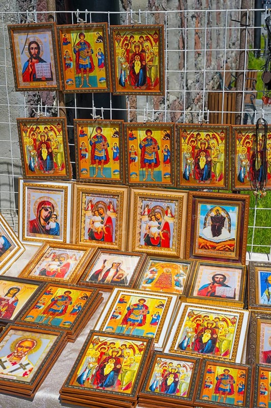 Icons in various frames with bright colors depict religious figures at a market stand, stand in front of the domed church of Kvemo Mleta Lomis, Kvemo Mleta, Mtskheta-Mtianeti region, Georgian Military Road, High Caucasus, Georgia