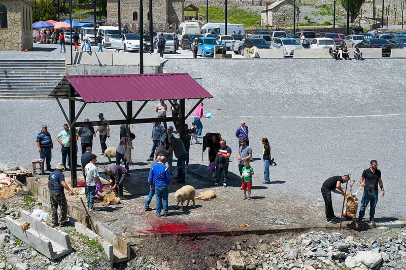 People gather around a slaughter site, bloody spots on the ground, parked cars, slaughter of sheep, Kvemo Mleta, Mtskheta-Mtianeti region, Georgian Military Highway, High Caucasus, Georgia