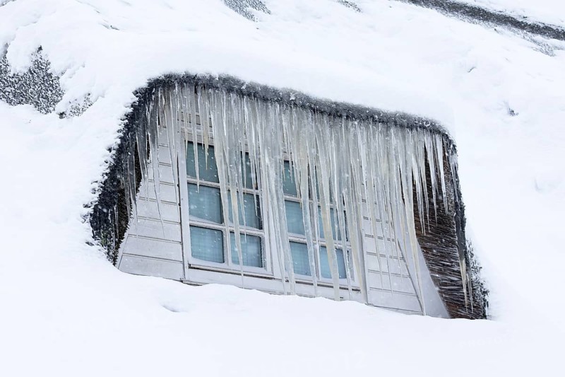 Icicles on a thatched roof covered with snow in front of a window in winter, Schleswig-Holstein, Germany