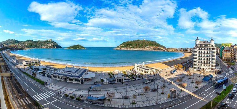 Panoramic view of la concha bay in san sebastian, spain, featuring the sandy beach, city architecture, and cantabrian sea under a blue sky with clouds, highlighting urban coastal beauty