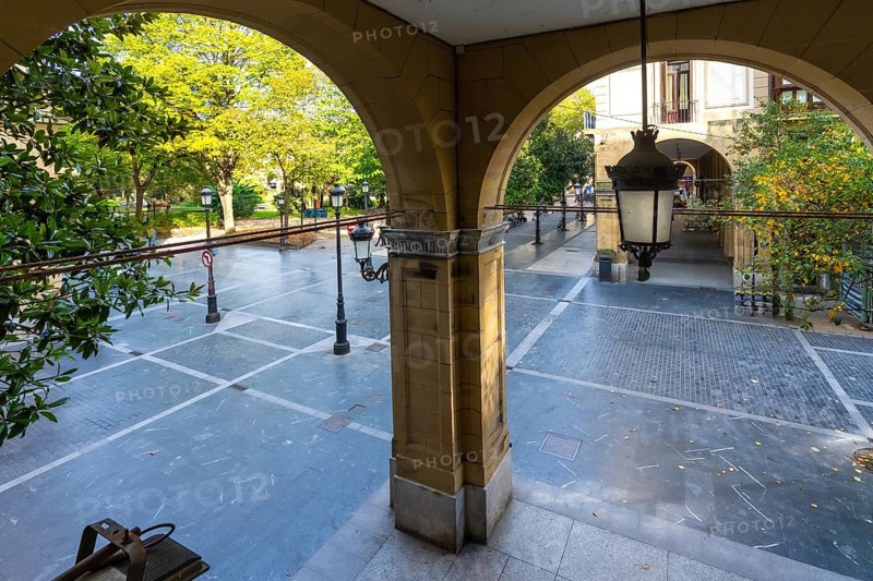 Arched arcade entrance providing a view through to gipuzkoa square park in san sebastian, featuring autumn trees, traditional street lamps, and historical architecture
