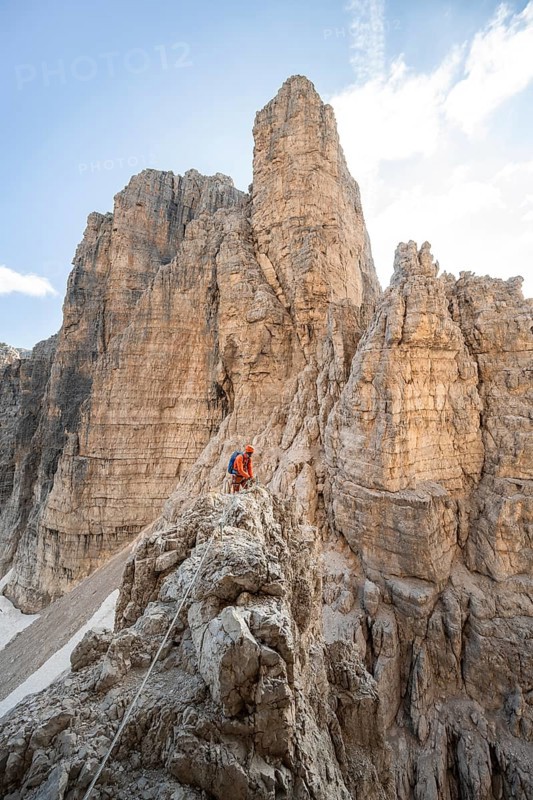 Mountaineer climbs an exposed rock in the secured Via Ferrata Bocciere Centrale via ferrata, spectacular rock towers in the back, Brenta Mountains, Brenta-Adamello Natural Park, Trentino, Italy