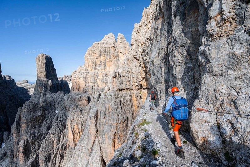Two mountaineers on an exposed rock band in the secured Via Ferrata Bocciere Centrale via ferrata, spectacular mountain landscape with steep rocky peaks, Brenta Mountains, Parco Naturale Brenta-Adamello, Trentino, Italy