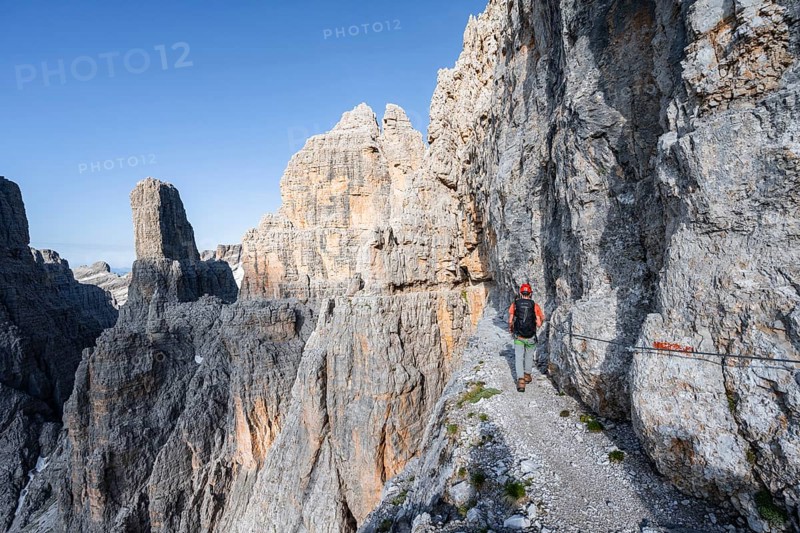 Mountaineers on an exposed rock band in the secured Via Ferrata Bocciere Centrale via ferrata, spectacular mountain landscape with steep rocky peaks, Brenta-Adamello Nature Park, Trentino, Italy