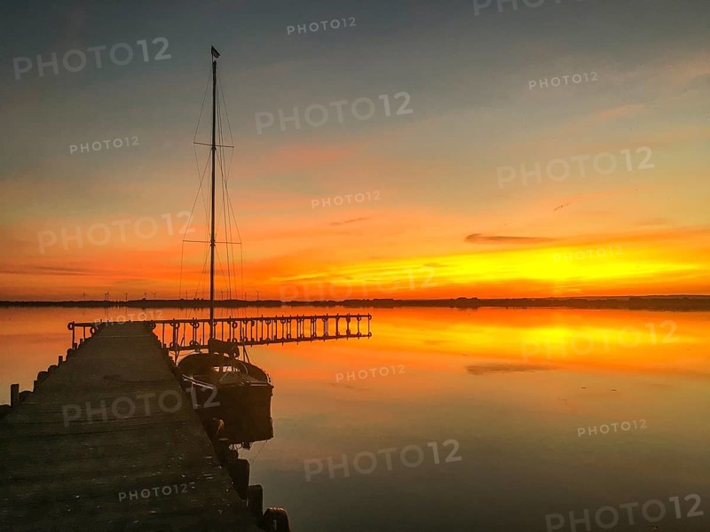 Tranquil Dümmer See with dock and sailboat at sunset, warm colors and calm atmosphere, Lembruch, Dümmer nature park Park, Lower Saxony, Germany