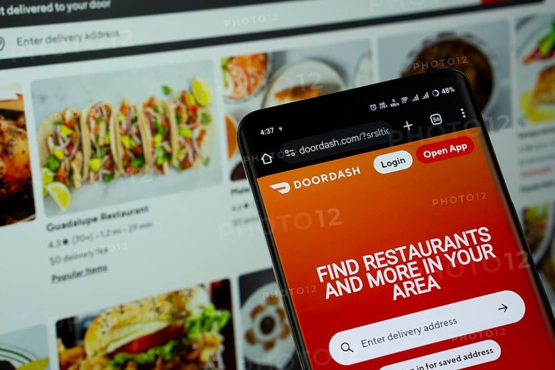 Dhaka, Bangladesh - 16 March 2025: The app of the DoorDash is displayed on a smartphone screen, and the website is visible on a computer screen in the background