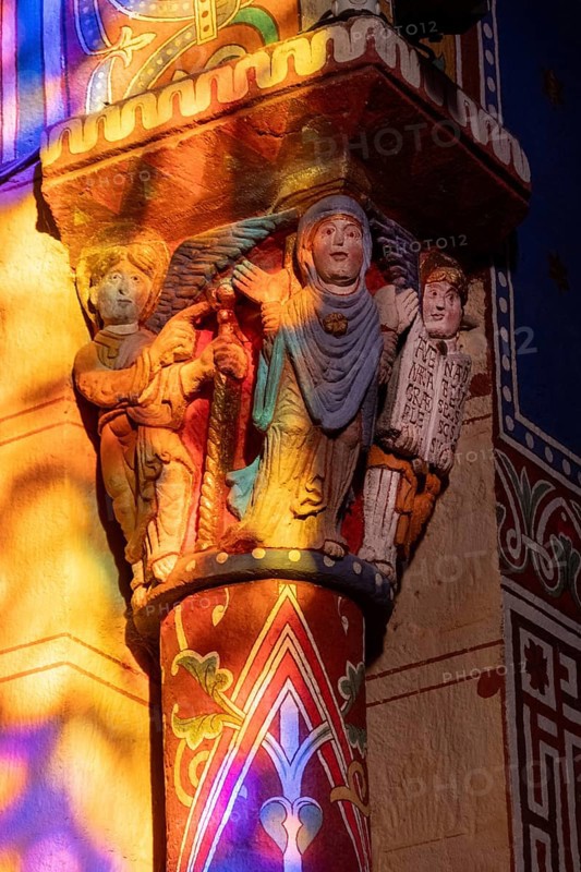 Issoire. Pillar (The Annunciation made to Mary) . The figures are illuminated by colorful light shining through a stained glass window inside Saint Austremoine Abbey, Puy de Dome, Auvergne Rhone Alpes, France