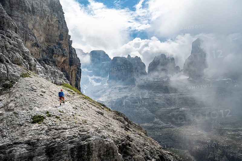 Mountaineers on a trail in front of picturesque mountain landscape with rocky peaks, Via Ferrata SOSAT via ferrata, Cima Tosa summit in the back, Brenta Mountains, Trentino, Italy