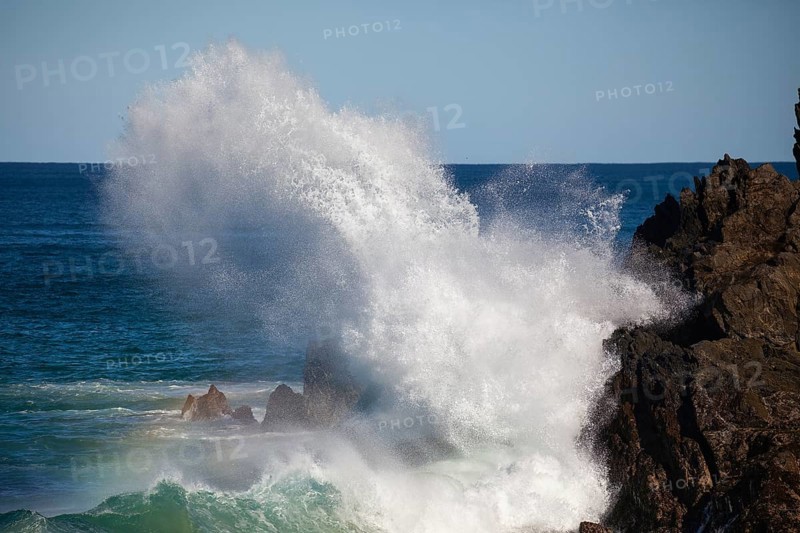 Waves crash against rocks at the mainland's easternmost point, creating rainbows in the ocean spray. Daylight, Byron Bay, New South Wales, Australia