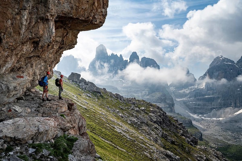 Two mountaineers on a path in front of a picturesque mountain landscape with rocky peaks, Via Ferrata SOSAT via ferrata, Cima Tosa summit in the back, Brenta Mountains, Trentino, Italy