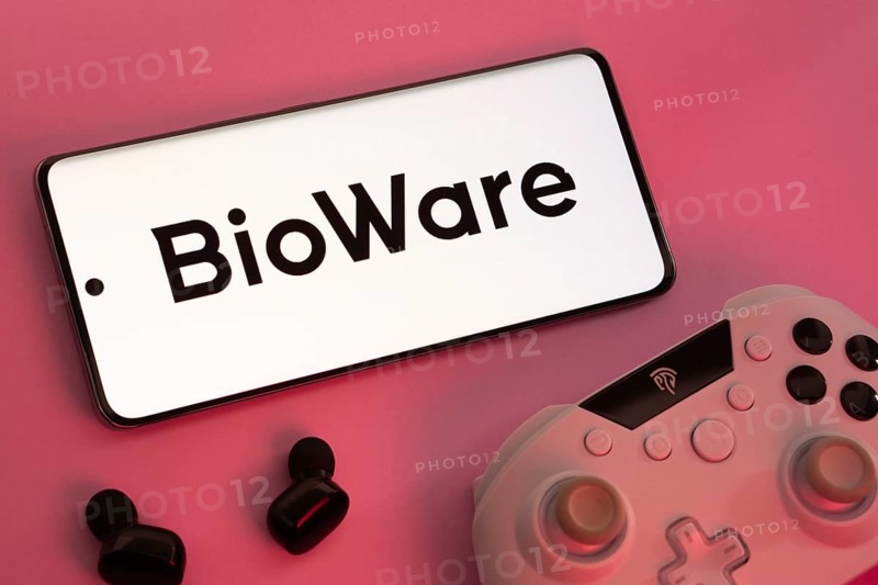 Dhaka, Bangladesh- 08 Apr 2025: A smartphone displaying the BioWare logo next to a gaming controller and earbuds on a pink surface