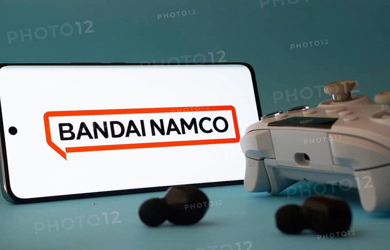 Dhaka, Bangladesh- 23 Mar 2025: A smartphone with a Bandai Namco Entertainment icon next to a controller and earbuds on a blue surface