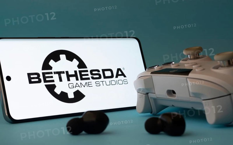 Dhaka, Bangladesh- 23 Mar 2025: A smartphone with a Bethesda Game Studios icon next to a controller and earbuds on a blue surface