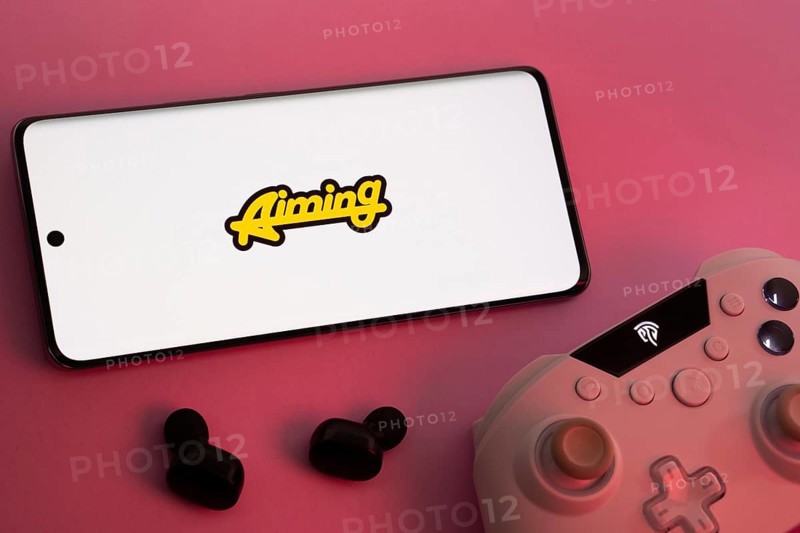Dhaka, Bangladesh- 08 Apr 2025: A smartphone displaying the Aiming Inc logo next to a gaming controller and earbuds on a pink surface