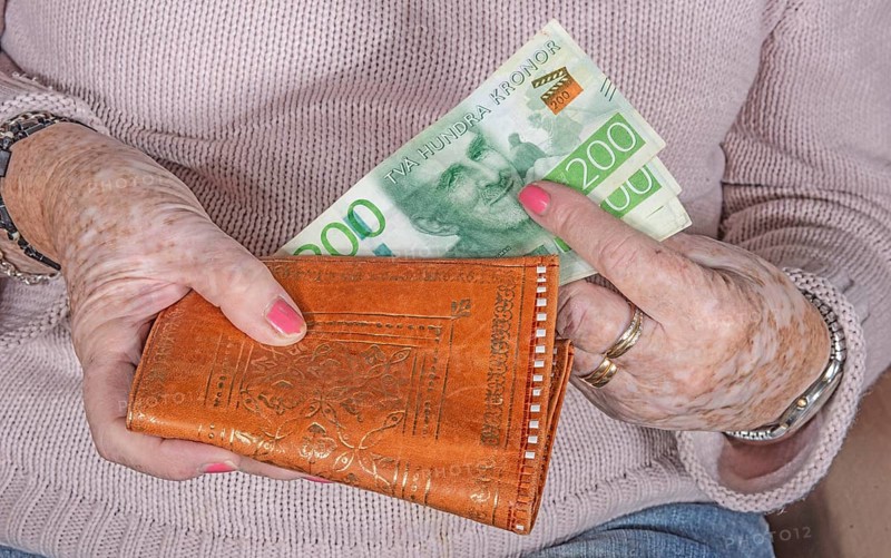 An elderly woman's hands take out Swedish banknotes from a wallet