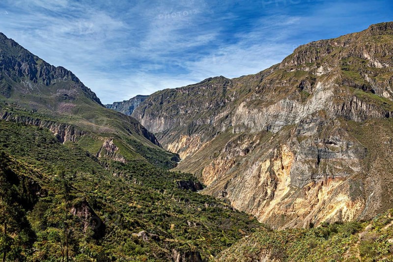Rocks surround a green valley under a wide sky, the landscape of Colca Canyon in the Aden of Peru
