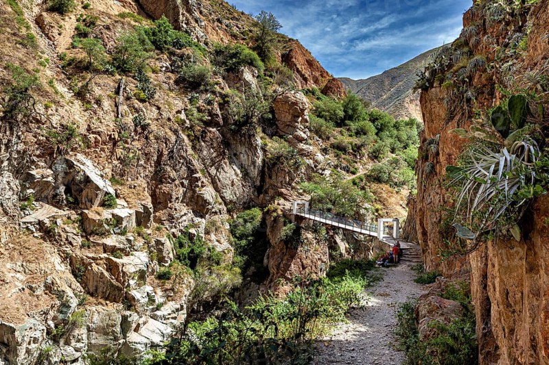 Trail leads along rocks to a suspension bridge, the landscape of the Colca Canyon in the Andes of Peru