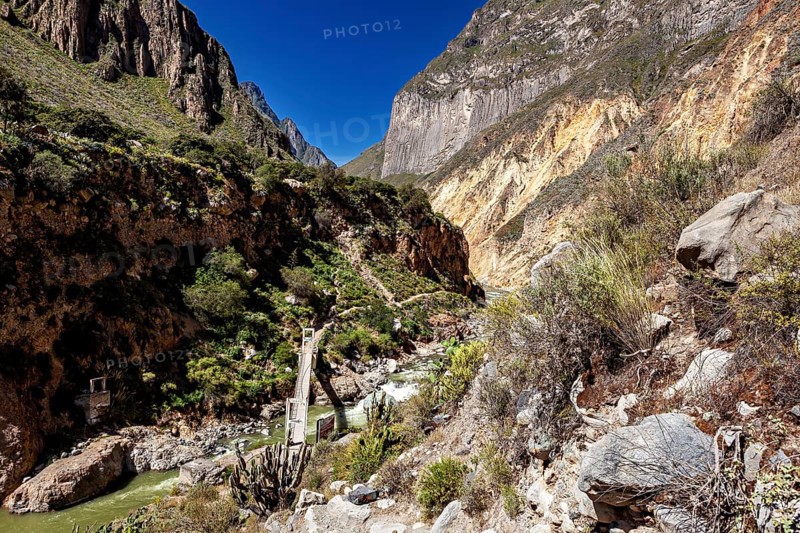 Suspension bridge spans river in deeply cut gorge with steep rocks, the landscape of Colca Canyon in the Aden of Peru