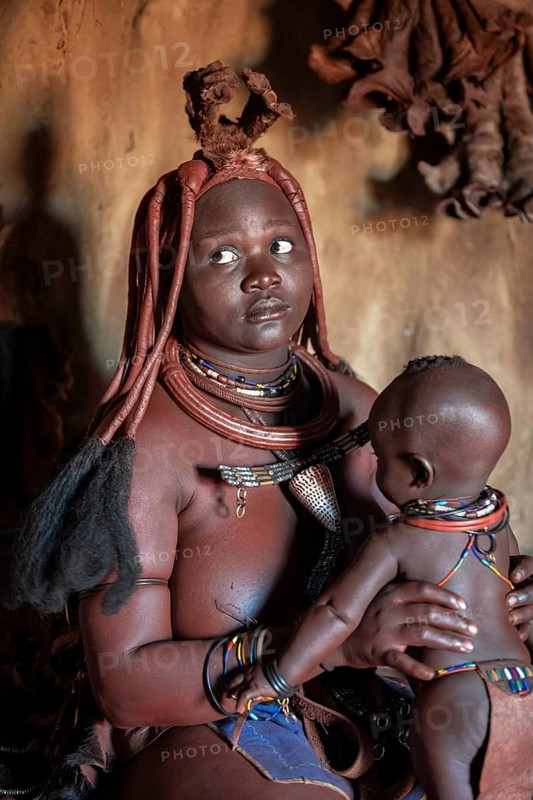 Himba woman sitting with baby in traditional hut, Himba village, Kaokoveld, Kunene, Namibia