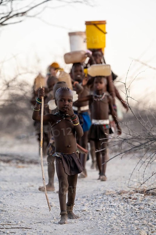 Himba woman and children run to fetch water with canisters through dry countryside, traditional Himba, Kaokoveld, Kunene, Namibia