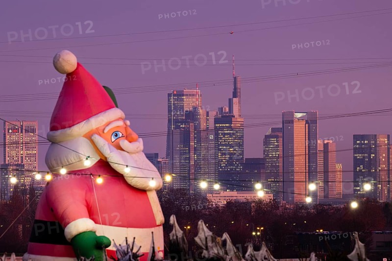 In a Christmas tree center near Frankfurt am Main, a multi-metre-high inflated figure of Santa Claus rises in front of the glowing banking skyline, Frankfurt am Main, Hesse, Germany