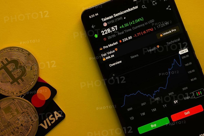 Dhaka, Bangladesh- 30 June 2025: Smartphone displaying TSMC stock data on a trading app with Bitcoin, Visa and Mastercard card on a vibrant yellow background
