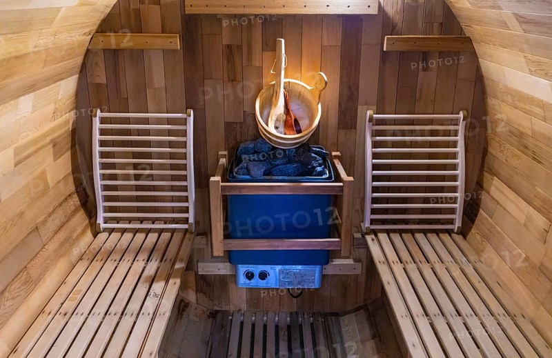 Steam and hot stone wooden cedar compact sauna interior with heating stone electrical device, hot water bucket and benches