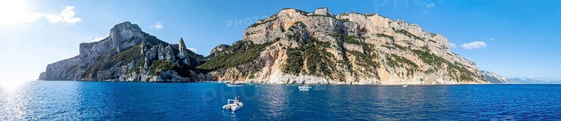 Couple on motorboat off picturesque rocky coast, cliffs with L'Aguglia pinnacle, blue sea and Cala Goloritzé beach, aerial view, Golfo di Orosei, Baunei, Sardinia, Italy