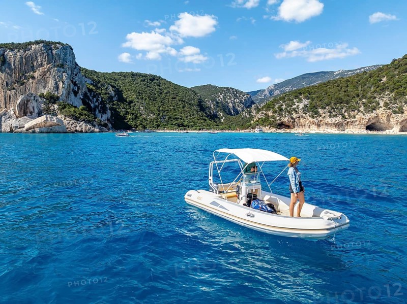 Motor boat off picturesque rocky coast, cliffs and Cala Luna beach, aerial view, Golfo di Orosei, Baunei, Sardinia, Italy