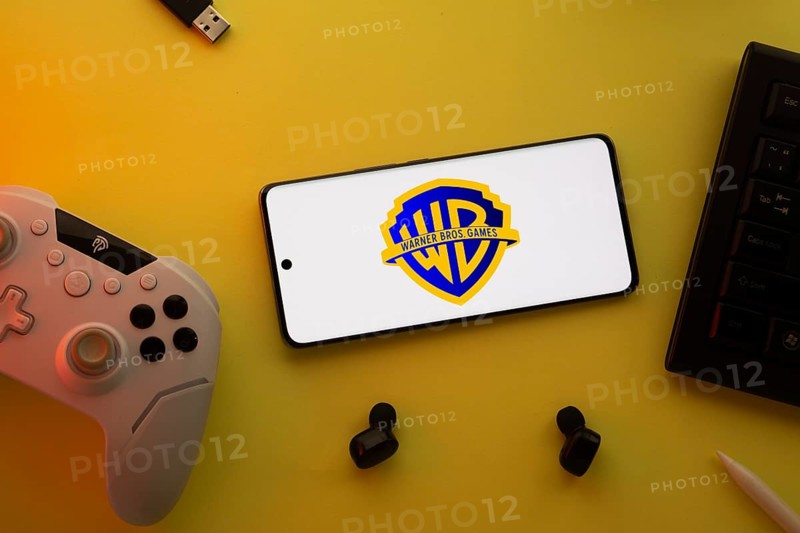 Dhaka, Bangladesh- 22 Mar 2025: Smartphone with Warner Bros. Games, game controller, and earbuds on a pink background