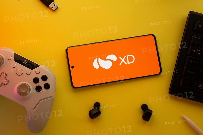 Dhaka, Bangladesh- 22 Mar 2025: Smartphone with XD logo, game controller, and earbuds on a pink background
