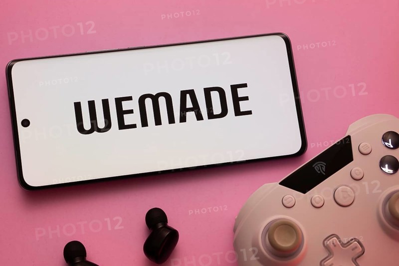 Dhaka, Bangladesh- 22 Mar 2025: Smartphone with WeMade Entertainment logo, game controller, and earbuds on a pink background
