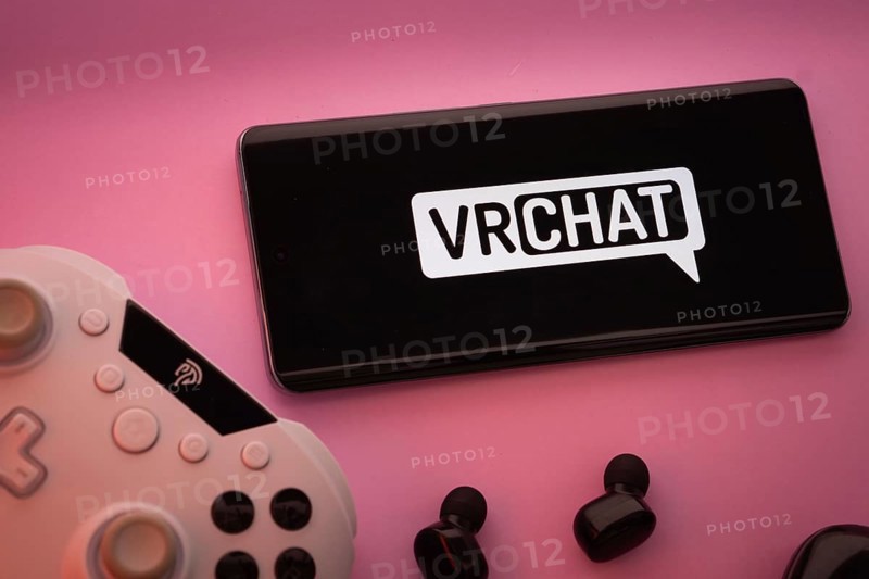 Dhaka, Bangladesh- 22 Mar 2025: Smartphone with VRChat logo, game controller, and earbuds on a pink background