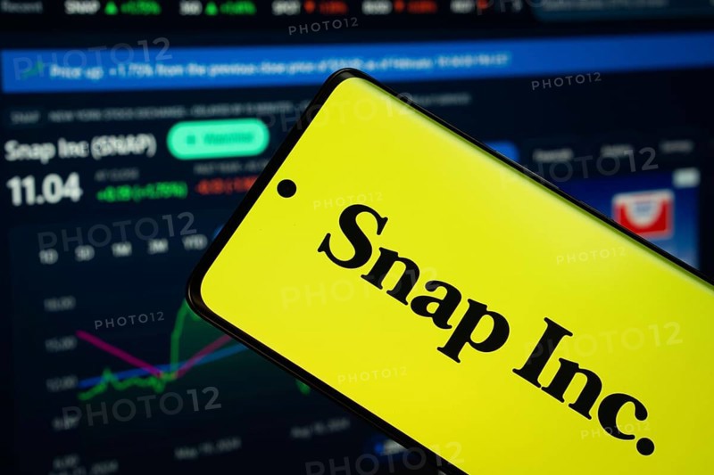 Dhaka, Bangladesh- 18 March 2025: Snap Inc logo is displayed on a smartphone screen, with a stock graph webpage visible on a computer screen in the background