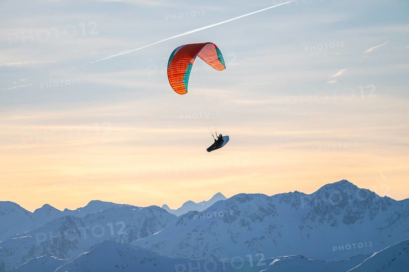 Paragliders flying over snowy mountain peaks in winter in evening light, Kitzbühel Alps, Tyrol, Austria