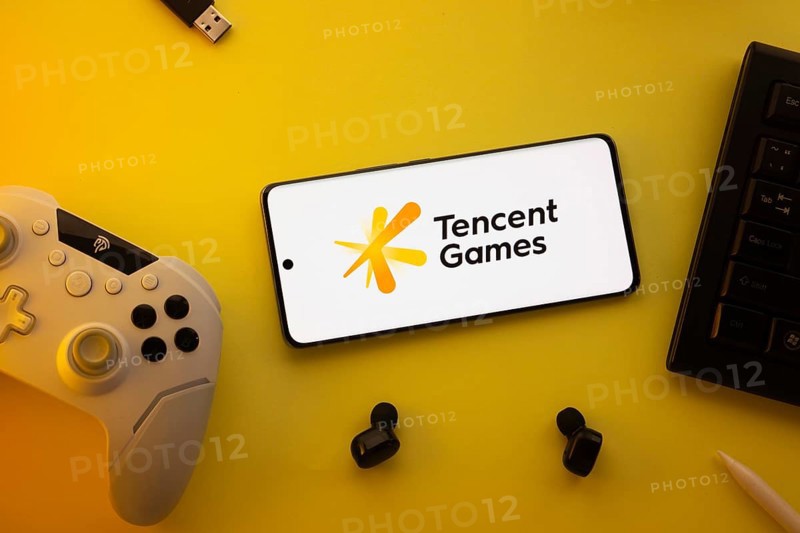 Dhaka, Bangladesh- 23 Mar 2025: Smartphone with Tencent Games logo, game controller, and earbuds on a yellow background