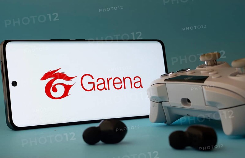Dhaka, Bangladesh- 23 Mar 2025: A smartphone with a Garena icon next to a controller and earbuds on a blue surface