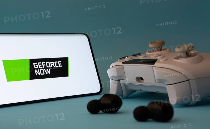 Dhaka, Bangladesh- 23 Mar 2025: A smartphone with a Geforce Now icon next to a controller and earbuds on a blue surface