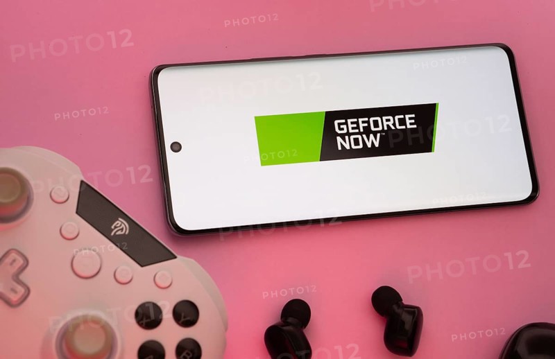 Dhaka, Bangladesh- 22 Mar 2025: Smartphone with Geforce Now logo, game controller, and earbuds on a pink background