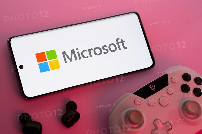 Dhaka, Bangladesh- 22 Mar 2025: Smartphone with Microsoft logo, game controller, and earbuds on a pink background
