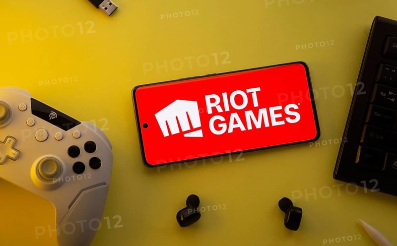 Dhaka, Bangladesh- 23 Mar 2025: Smartphone with Riot Games logo, game controller, and earbuds on a yellow background