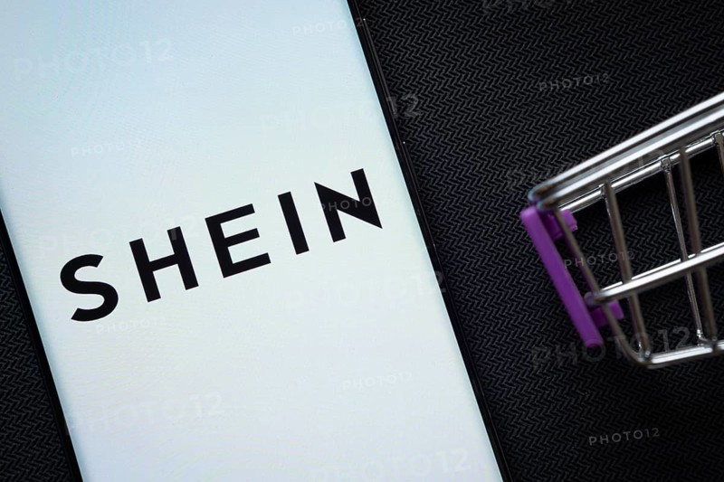 Dhaka, Bangladesh- 03 July 2025: A smartphone displaying the SHEIN logo next to a miniature shopping cart on a background