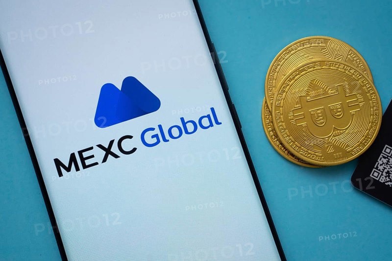 Dhaka, Bangladesh- 03 Sep 2025: MEXC Global logo on smartphone screen near Bitcoin coin and QR code on blue background