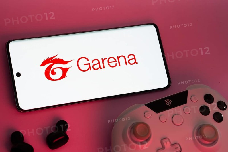 Dhaka, Bangladesh- 22 Mar 2025: Smartphone with Garena logo, game controller, and earbuds on a pink background