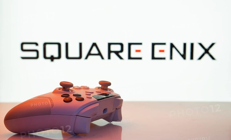 Dhaka, Bangladesh- 14 Nov 2025: A close-up of a white gamepad with the Square Enix seen on screen in the background