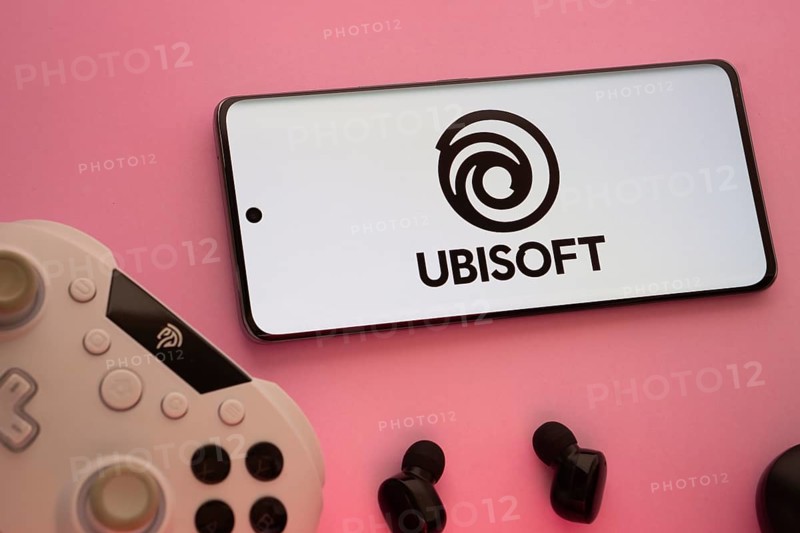 Dhaka, Bangladesh- 22 Mar 2025: Smartphone with Ubisoft logo, game controller, and earbuds on a pink background