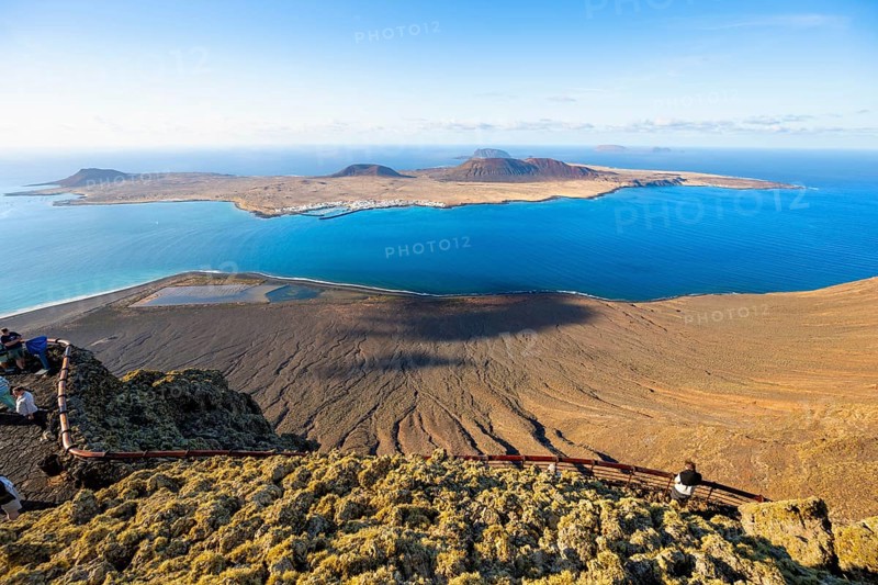 View of La Graciosa island with volcanic craters in the evening light, tourists on an observation deck at the Mirador del Río viewpoint designed by artist César Manrique, Lanzarote, Canary Islands, Spain