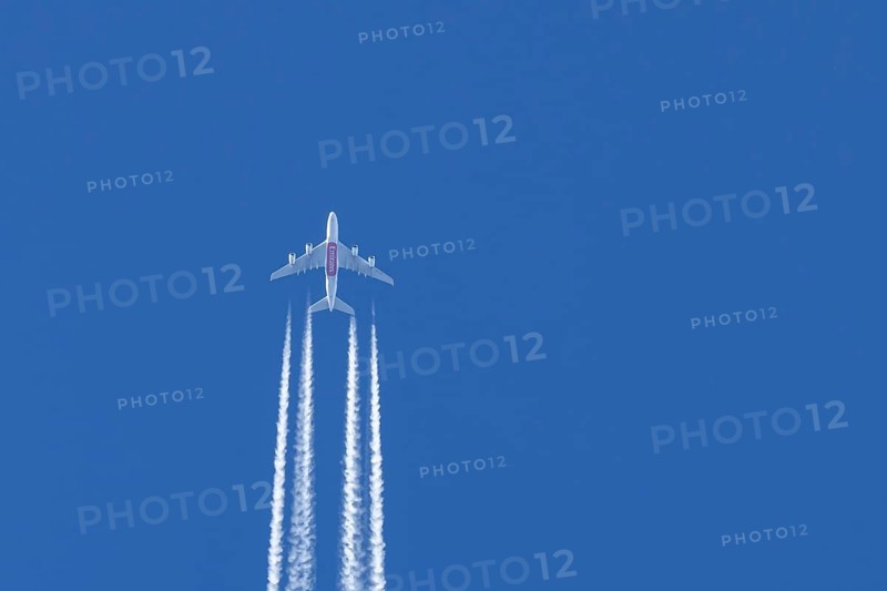 Airbus A380 jet passenger aircraft of Emirates airlines flying in a blue sky with contrails or vapour trails behind, England, United Kingdom