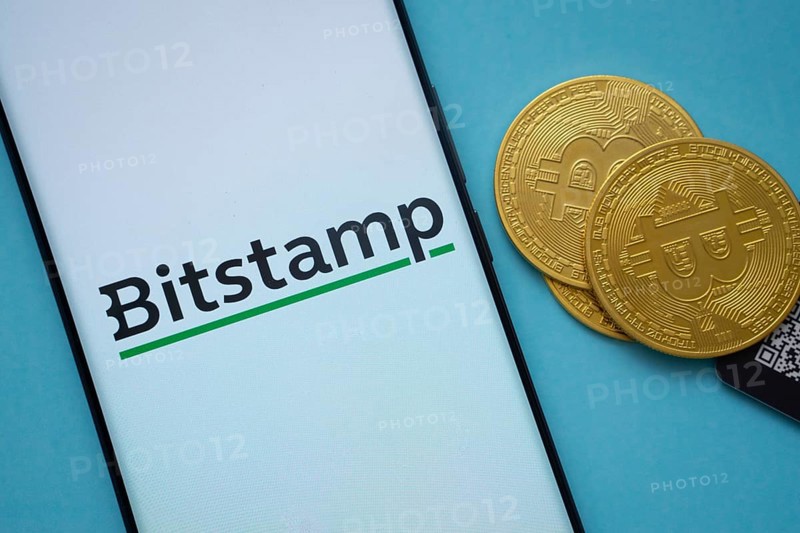 Dhaka, Bangladesh- 03 Sep 2025: Bitstamp logo on smartphone screen near Bitcoin coin and QR code on blue background